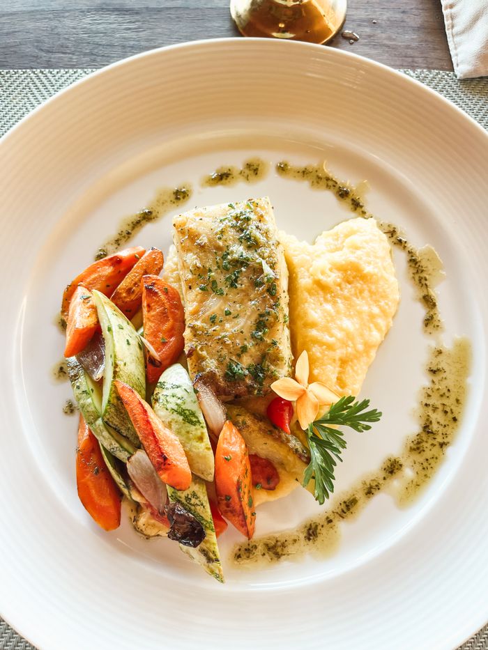 A gourmet salmon dish plated with roasted vegetables and a side of creamy polenta.