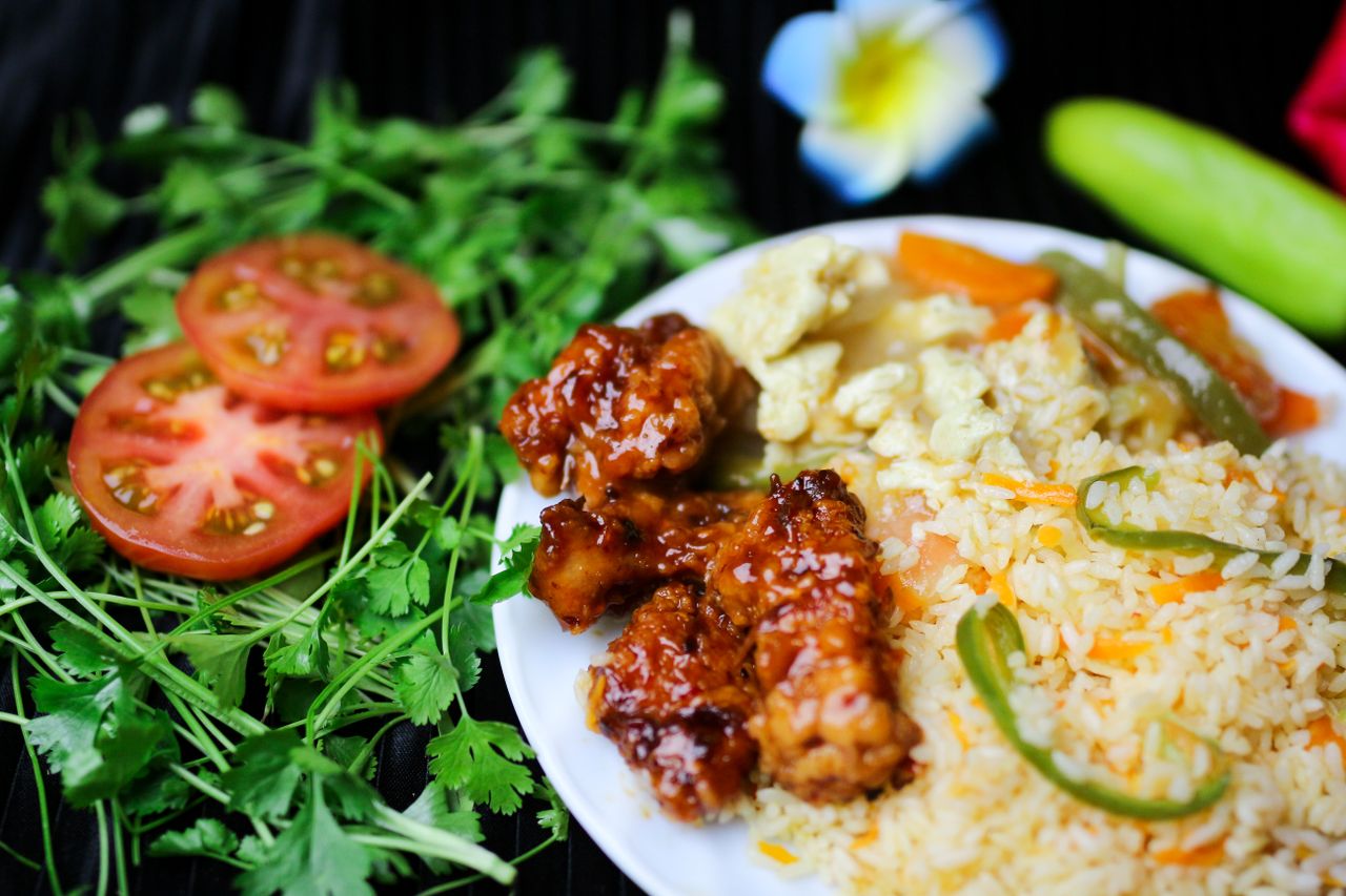 A vibrant Asian fusion dish with fried rice, glazed chicken, and fresh vegetables, garnished with cilantro.
